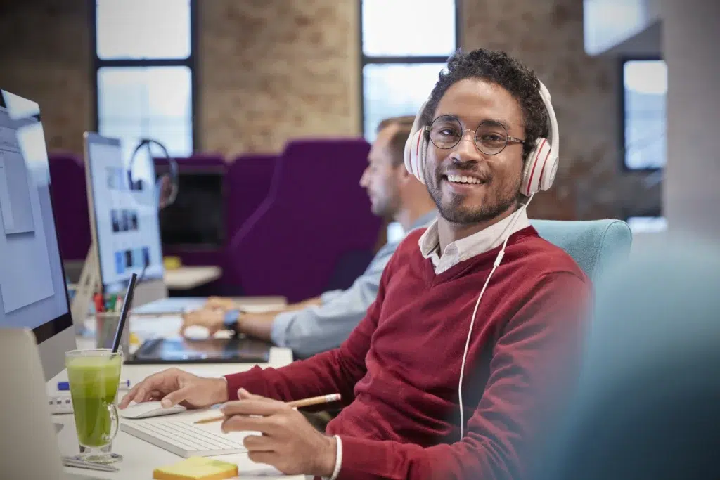 Hire Remote Developers in 2026: Why the Nearshore Model is Outperforming Offshore Teams 3 Cheerful young man with headphones at his desk, suitable to hire remote developers.