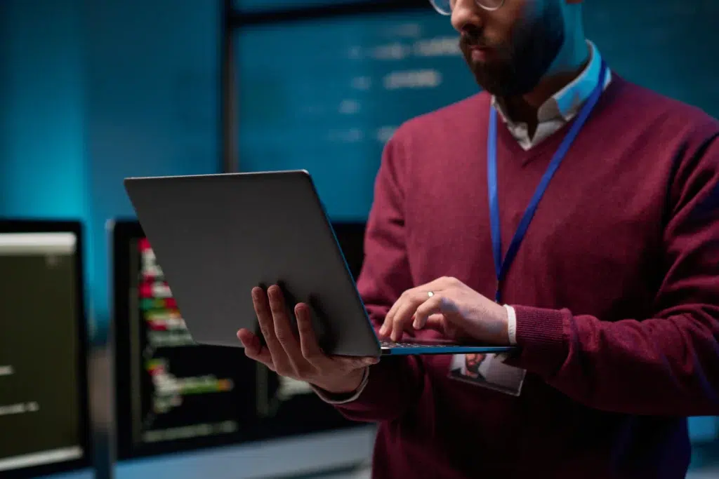 Software engineer remote holding laptop in front of server and code screens