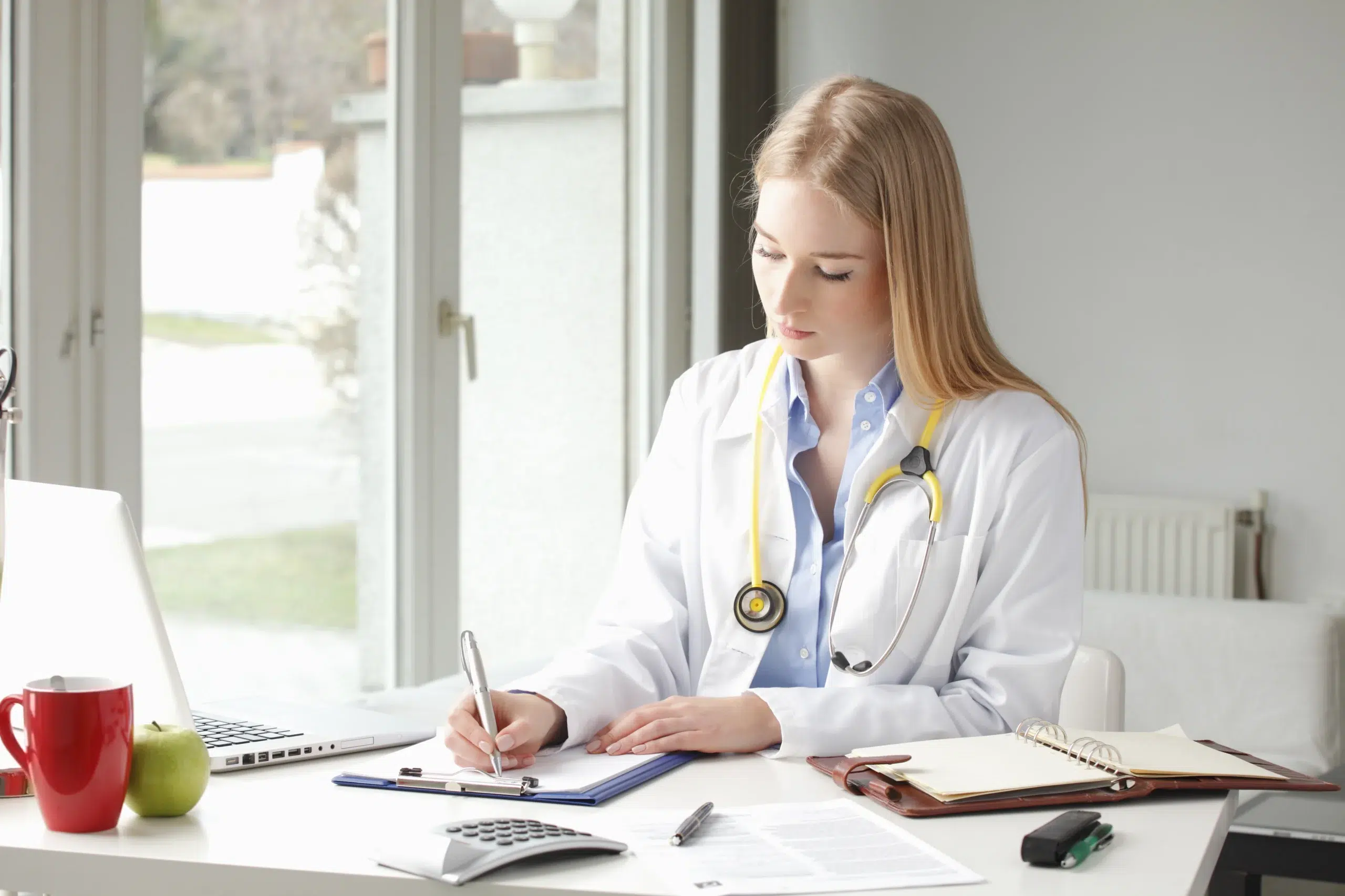 Physician documenting prior authorization requests at her desk