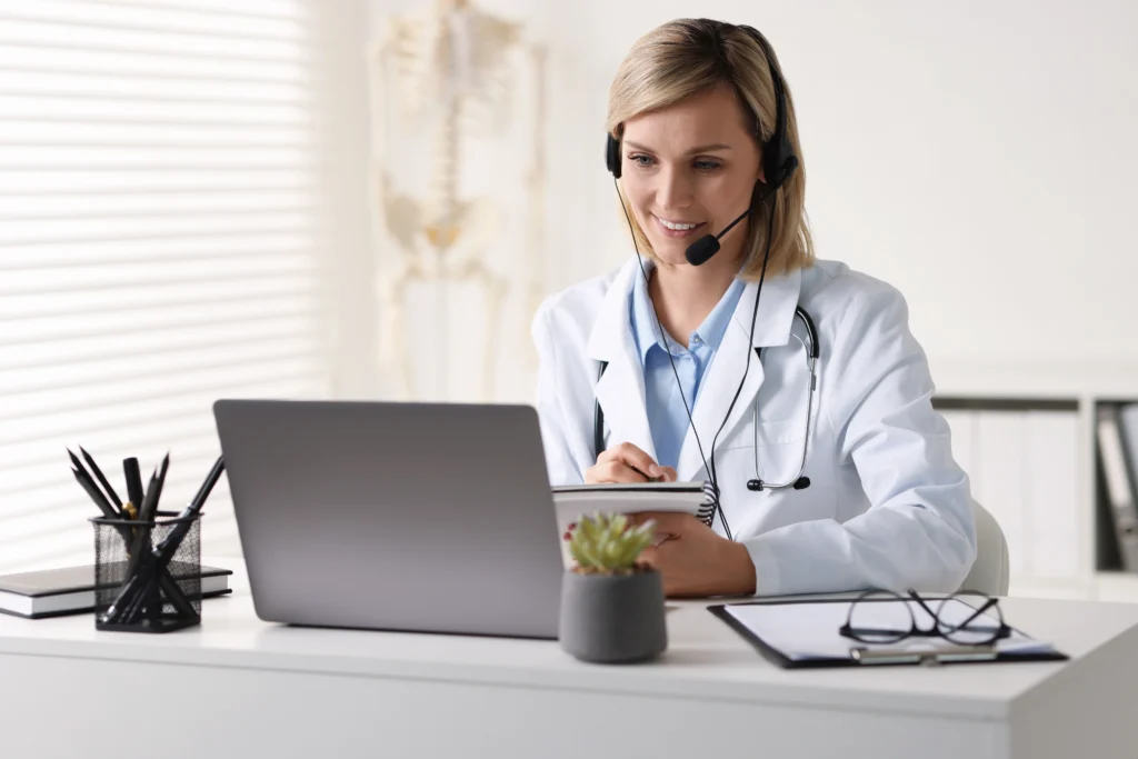 Smiling doctor reviewing patient records on a laptop during a visit eligible for the G2211 CPT code add-on