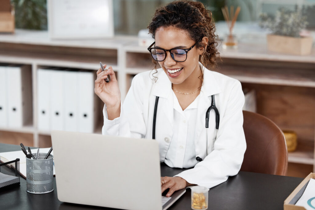 Smiling doctor using a laptop in her office while reviewing an outsourcing implementation plan for RCM operations