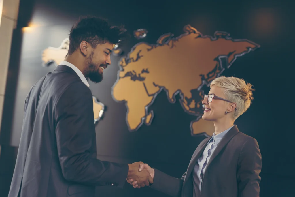 Business professionals shaking hands at the workplace in front of a world map, symbolizing a nearshore outsourcing agreement in Latin America